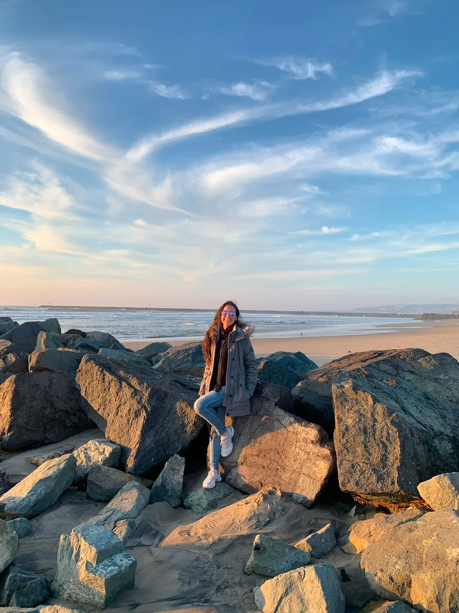 Julia sentada nas pedras de uma praia, no fim da tarde